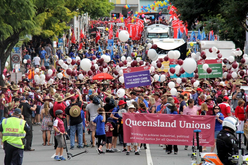 Thousands of union members with balloons and banners congregate together on a street.