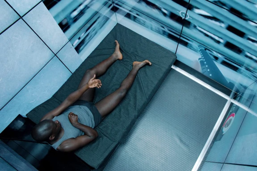 A man lying down on a grey bed with screens all around him