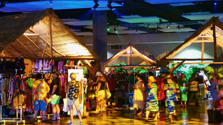 People dressed in colourful clothing walk between various displays at the FestPAC village.