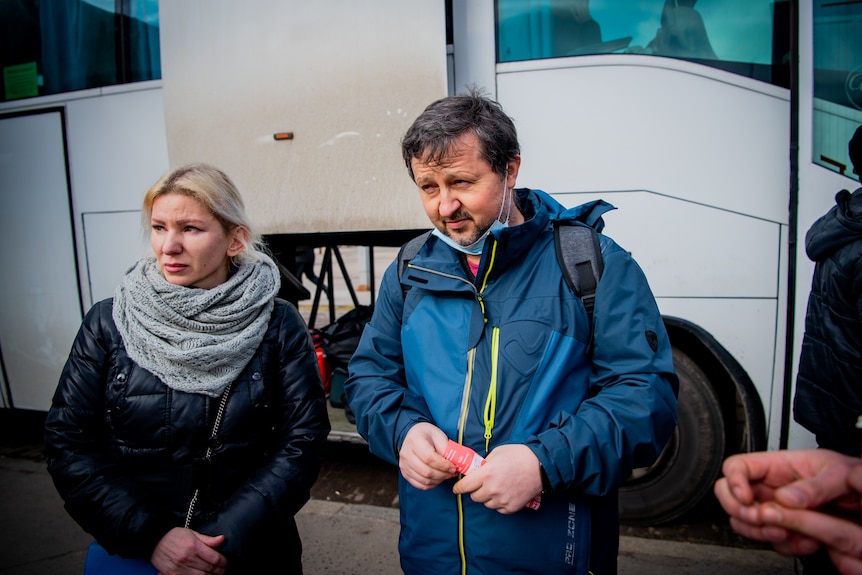 A man dressed in a blue jacket looks away with a woman next to him.