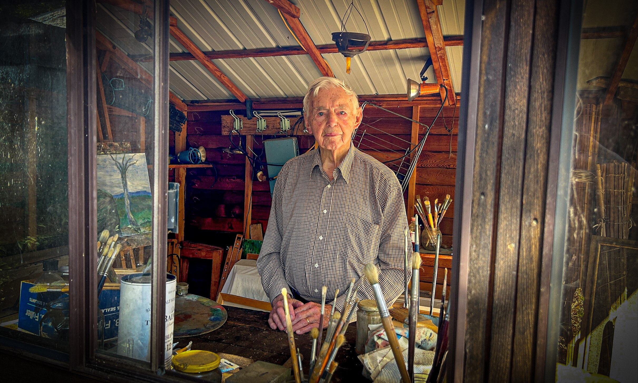 A man stands in an art studio looking at the camera through an open window.