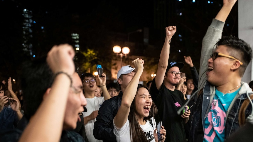 A crowd of Hongkongers at night raise their firsts in the air and cheer.