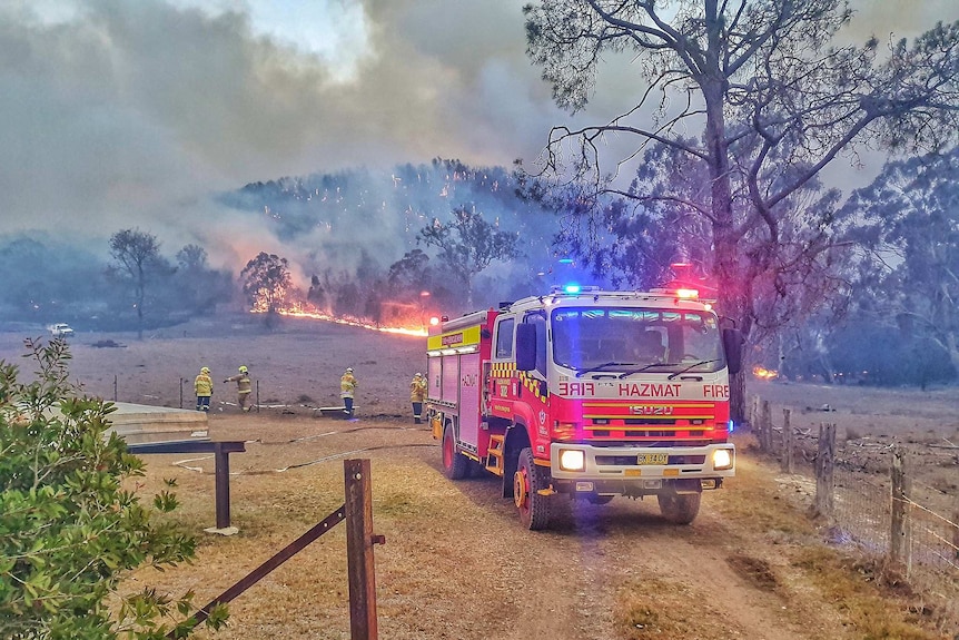 A fire truck and firefighters in front of burning bushland.