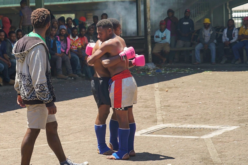 Two men embrace, while the crowd and official looks on.