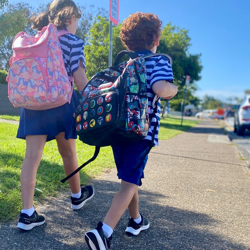 Two young school children walk towards school carrying colourful backpacks.
