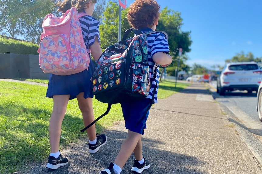Two young school children walk towards school carrying colourful backpacks.