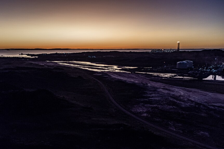 The sun sets on the Scarborough gas plant, coastline in the foreground.