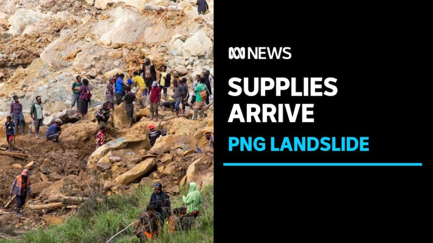 Supplies Arrive, PNG Landslide: Wideshot of people standing on rubble from a landslide.