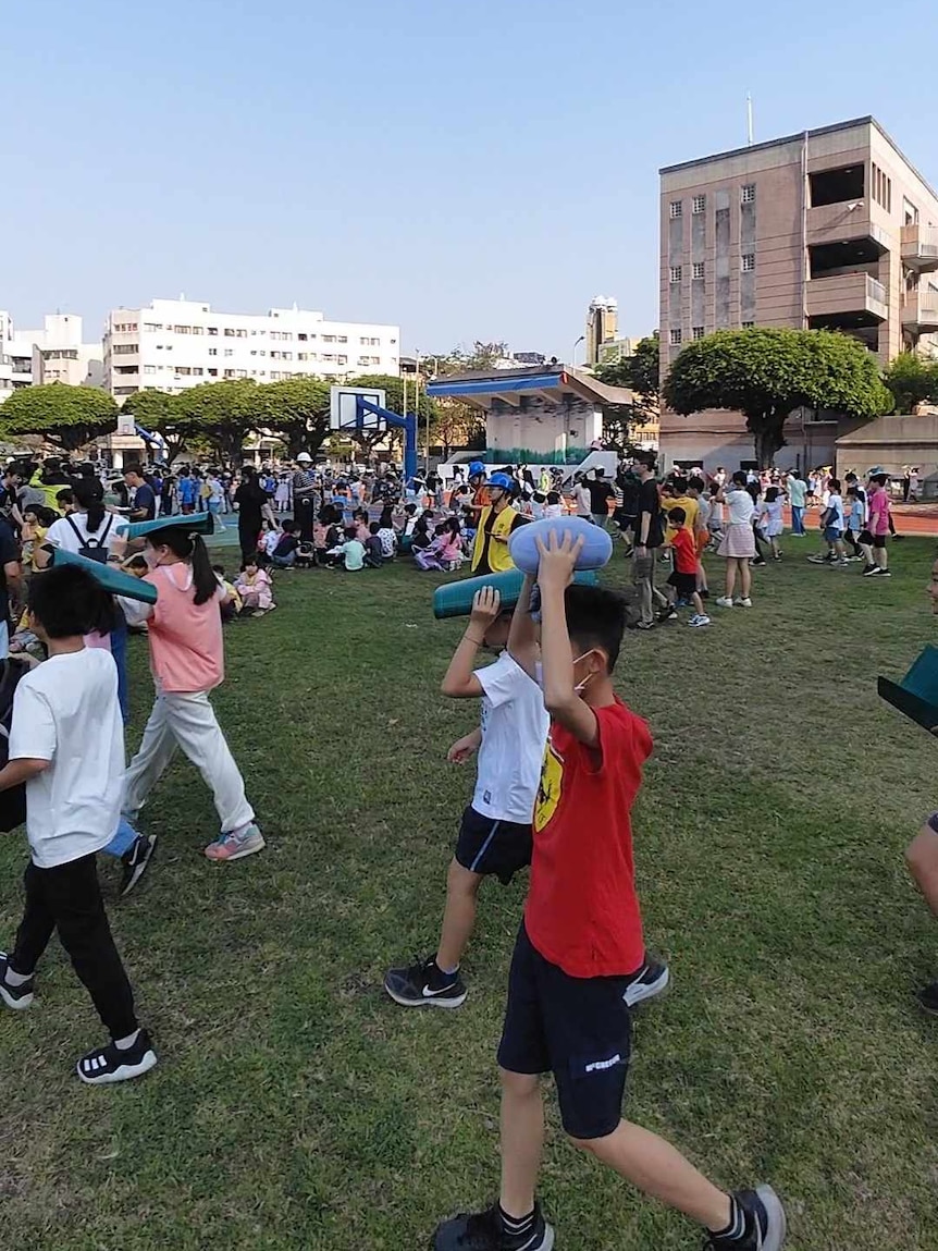 Crowds of kids holding objects like balls and books above their head as they walk onto green grass