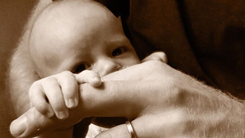 A sepia toned image of a baby holding on to its dads finger