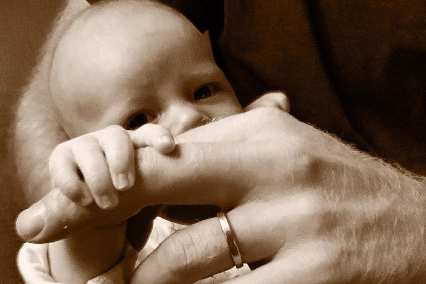 A sepia toned image of a baby holding on to its dads finger