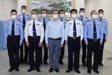 A group of uniformed men standard in a row inside an office space.