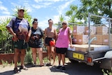 A tall Aboriginal man, two young Aboriginal women and an older Aboriginal woman standing next to a trailer containing boxes
