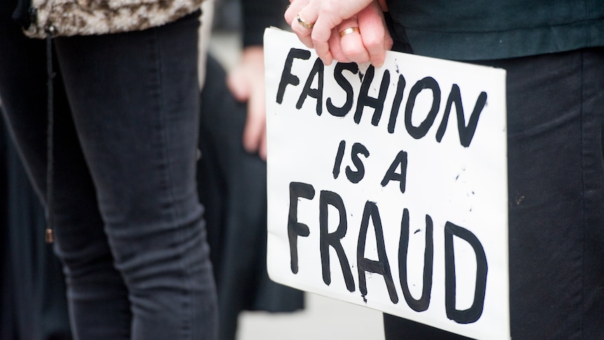 Hands hold a sign that reads 'FASHION IS A FRAUD'.