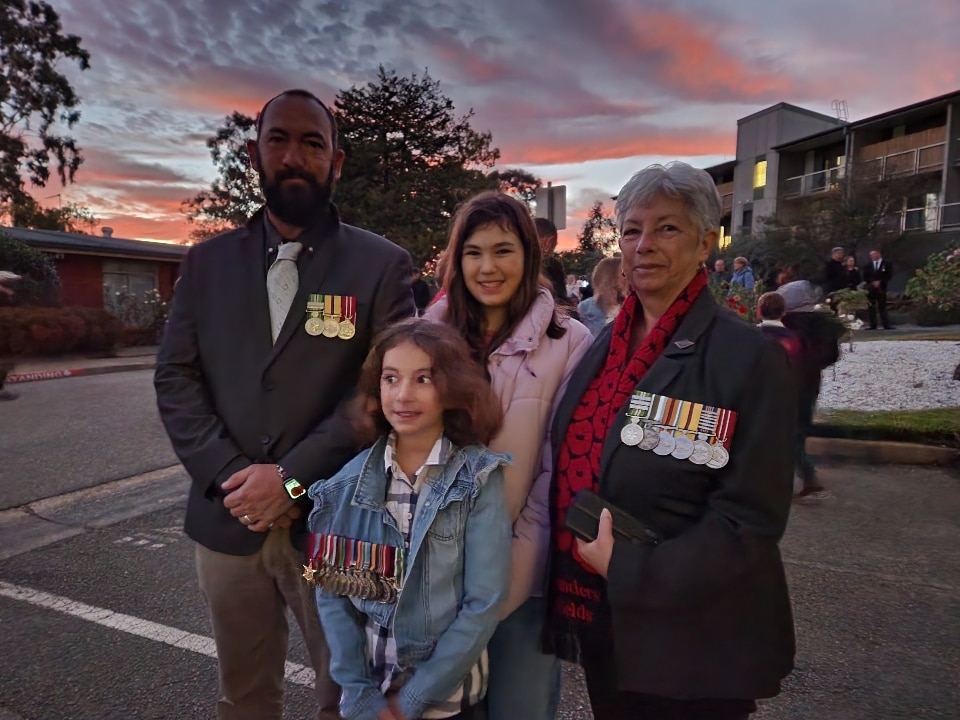 An older man and an older woman wearing war medals stand with two children at sunrise.
