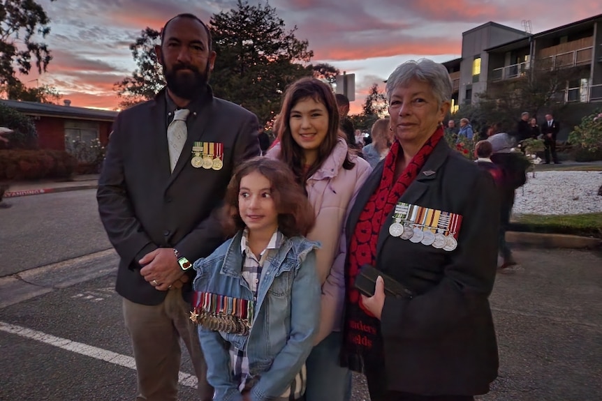 An older man and an older woman wearing war medals stand with two children at sunrise.