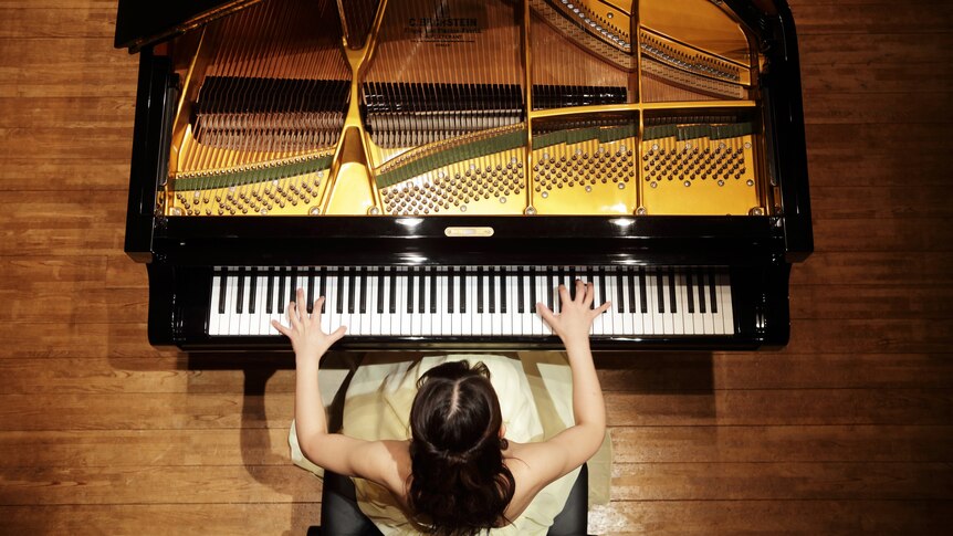 photo taken from above of a woman playing a grand piano