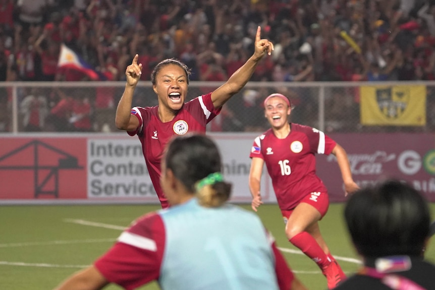 A Philippines women's footballer has arms raised and cheers
