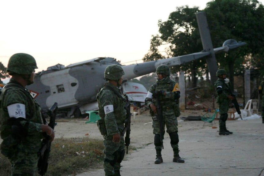 Soldiers stand guard next to a military helicopter which crashed on top of two vans in an open field