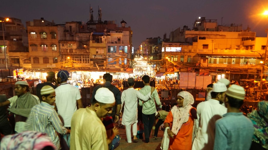 A crowd walks down a hill towards a busy street at night.