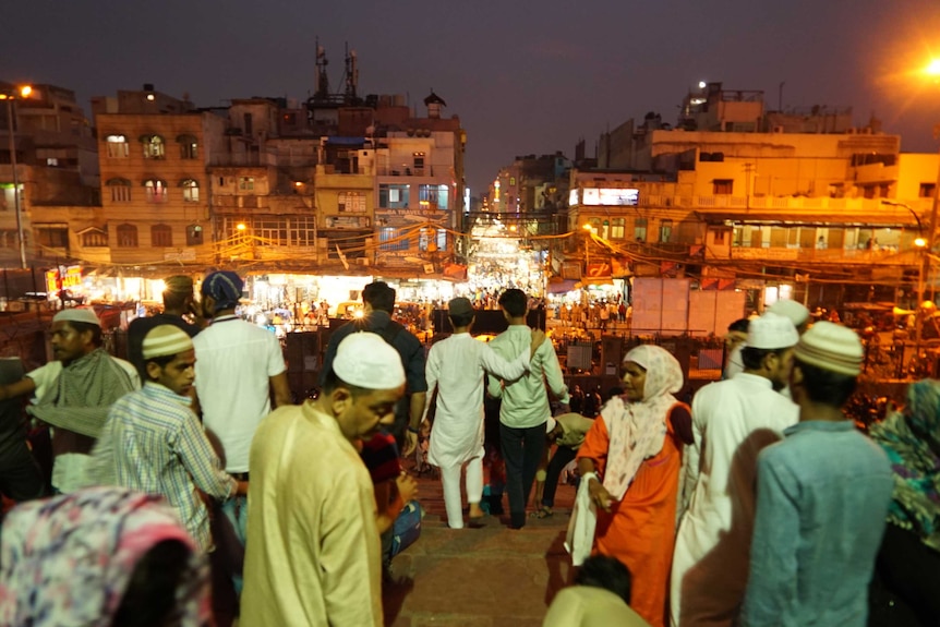A crowd walks down a hill towards a busy street at night.