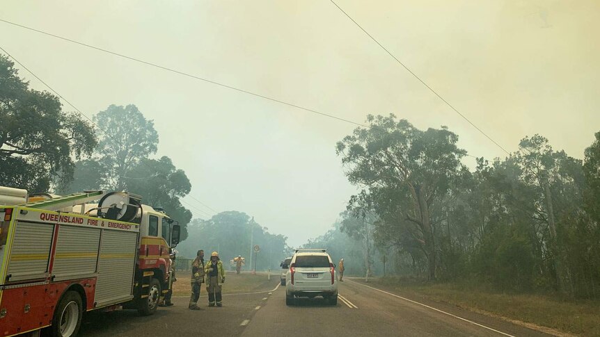 Fire authorities and a truck on a smoke-covered road at the scene of the bushfire at Cooroibah.