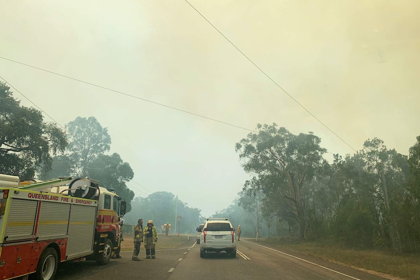 Fire authorities and a truck on a smoke-covered road at the scene of the bushfire at Cooroibah.