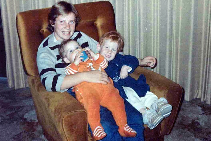 Ursula, as a girl, sits in an armchair holding two young children.
