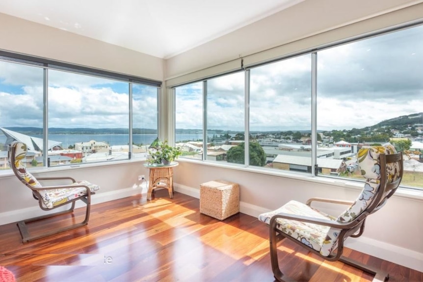 A picturesque view of the ocean from a second-storey living room with large glass windows and wooden floors.
