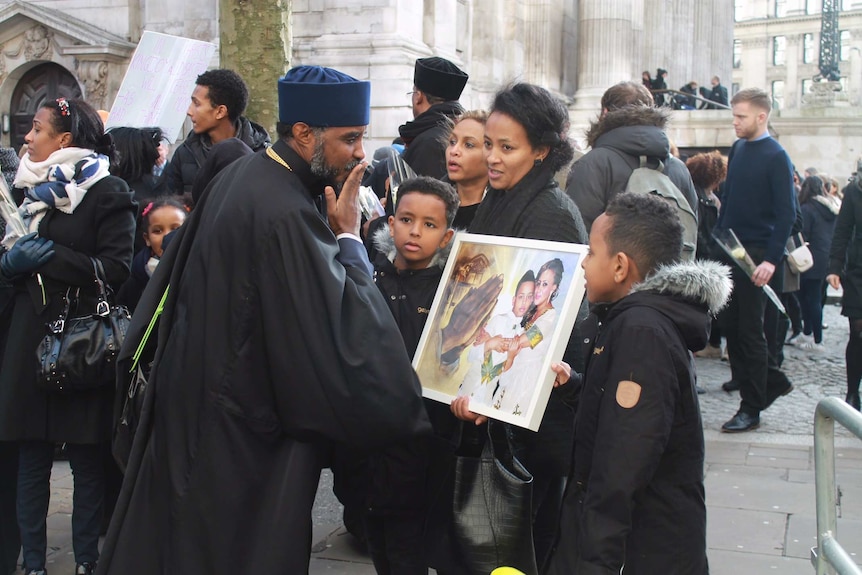 A cleric blesses a family holding a photograph.