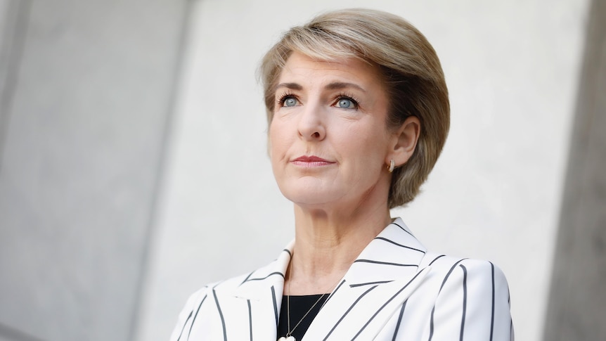 A woman with blonde hair  looking upward wearing a black and white striped blazer