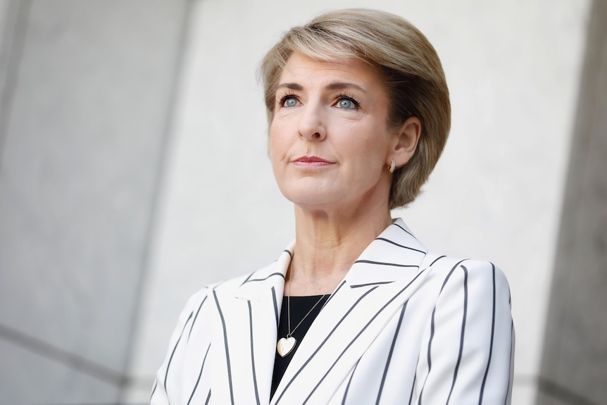 A woman with blonde hair  looking upward wearing a black and white striped blazer