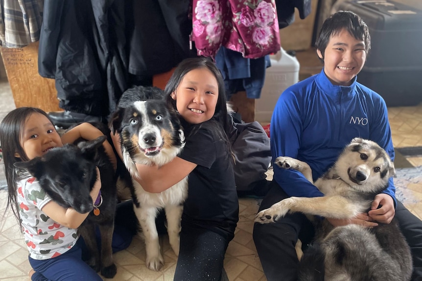 Three children smiling as they cuddle their three dogs.