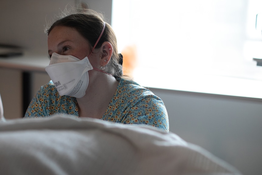 Bailey tilts her head as she looks towards someone off camera, her smiling eyes are seen above her face mask.