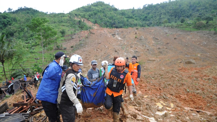 Rescuers carry the body of a landslide victim wrapped in a blue tarp