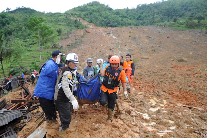 Rescuers carry the body of a landslide victim wrapped in a blue tarp