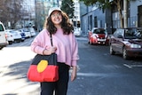 Hannah Donnelly stands on the street in Melbourne in a pink sweater and Aboriginal flag bag.