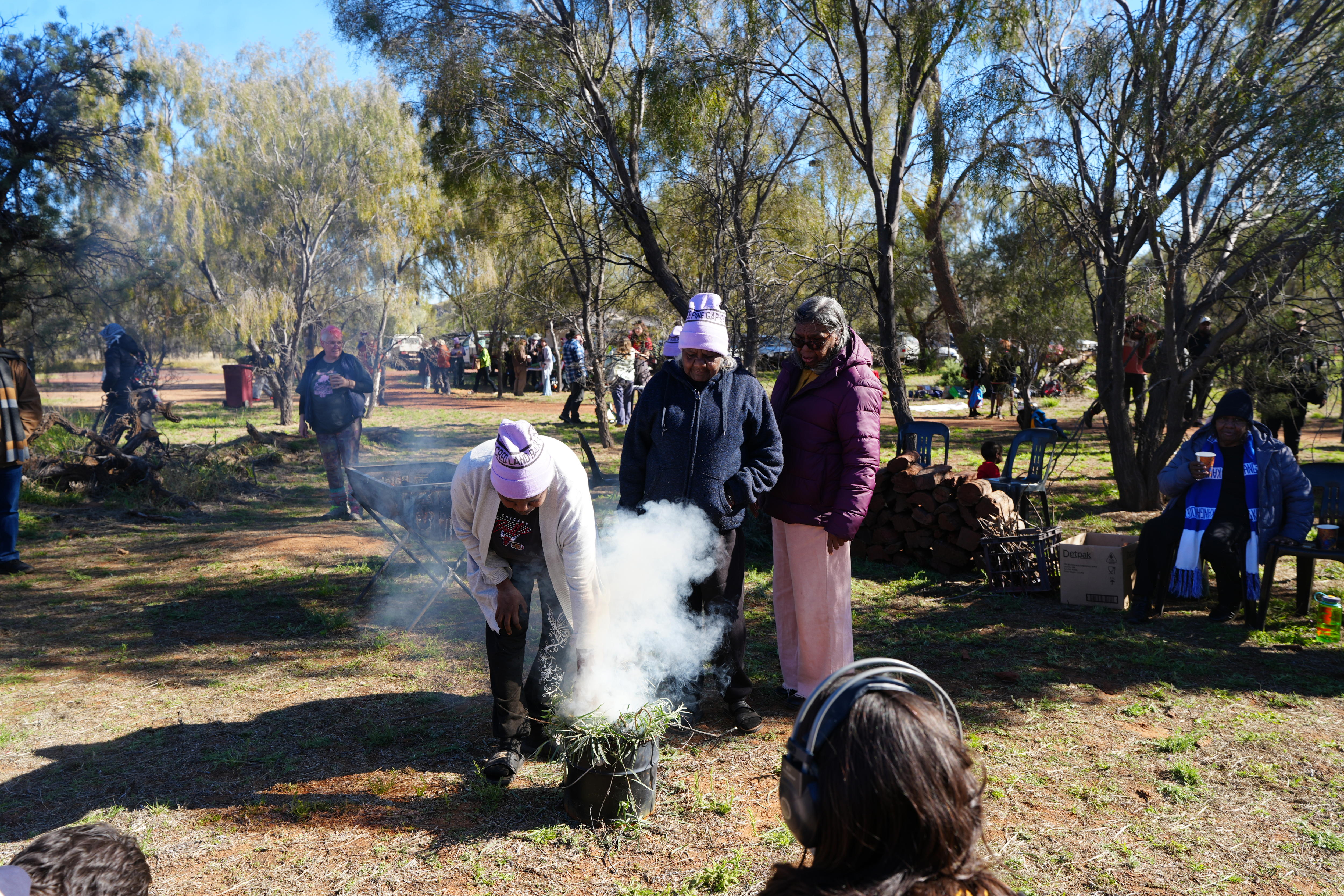 Three women stand around a bucket full of burning gum leaves.