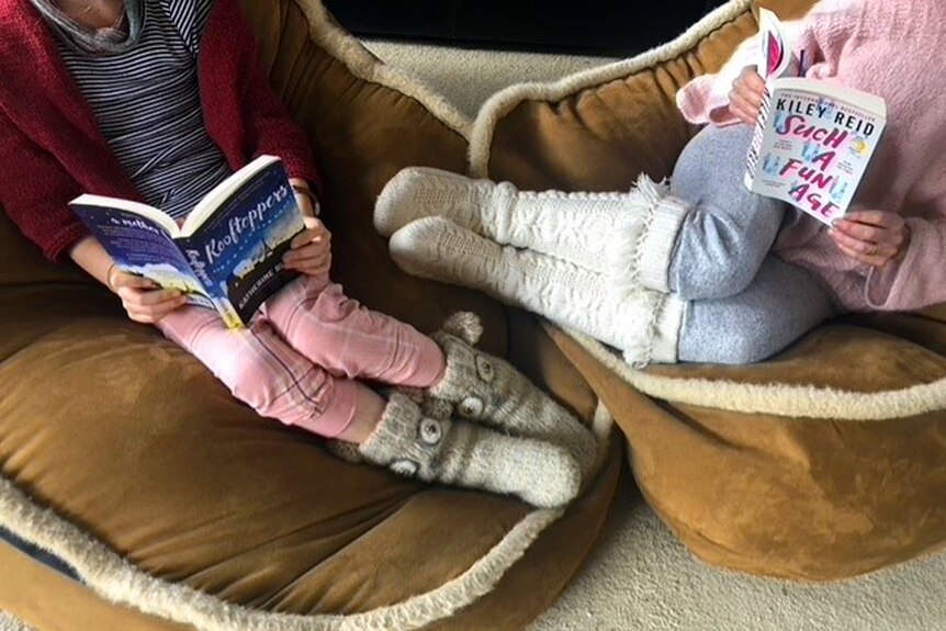 Two girls wearing slippers relaxing in armchairs, reading books.