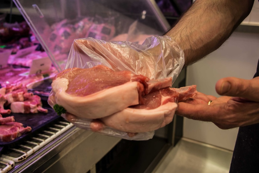 Melbourne butcher Tony Montesano holds up two steaks, using a plastic bag to cover his hand.