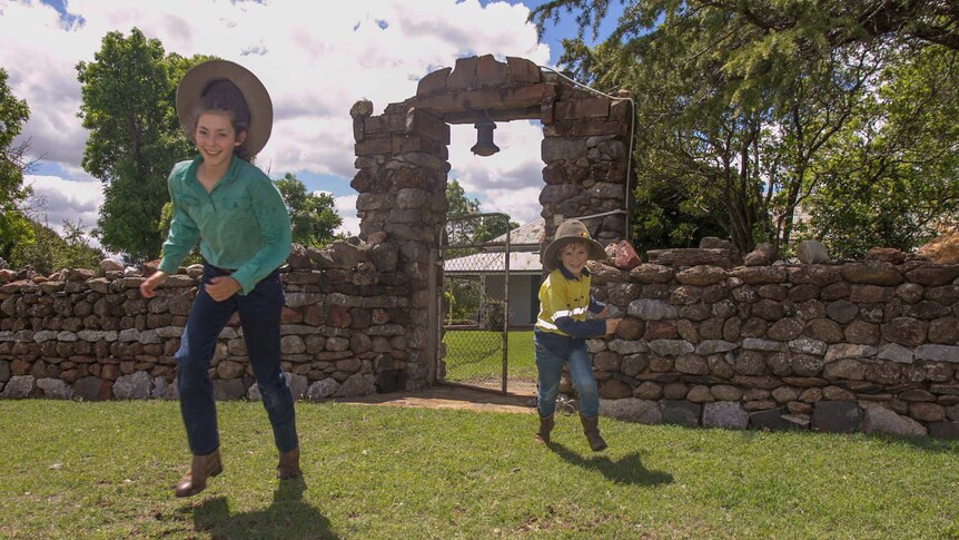 Two children in farm gear running through an old stone gate