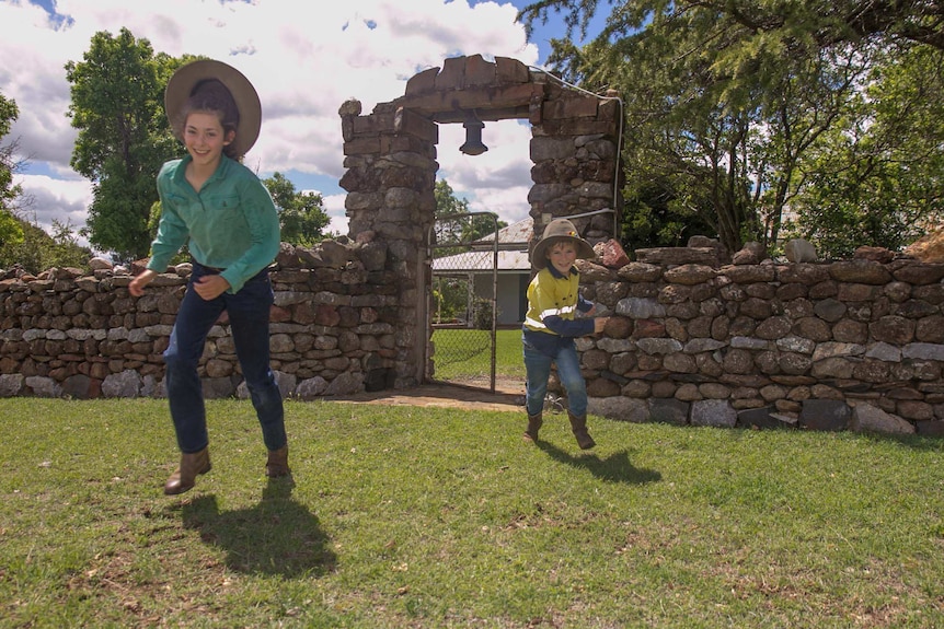 Two children in farm gear running through an old stone gate