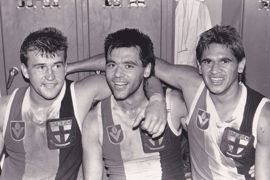 Three men in St Kilda jerseys put their arms around one another.