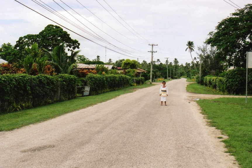 Child standing in the middle of the road between lush green corridor.