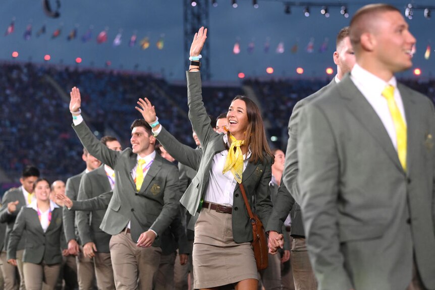 australian athletes smile and wave wile walking through a stadium at the commonwealth games opening ceremony