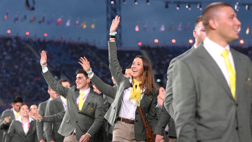 australian athletes smile and wave wile walking through a stadium at the commonwealth games opening ceremony