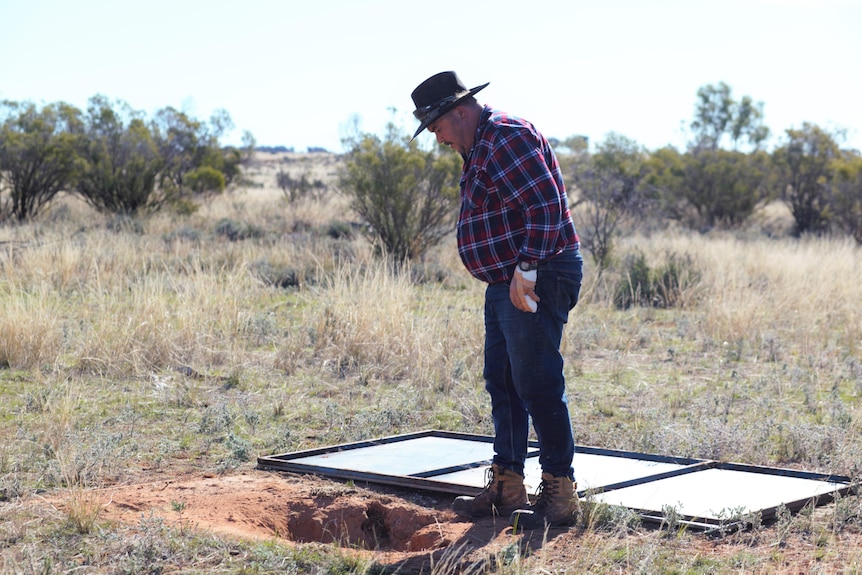 A man in a checked shirt looks into a hole in the ground approximately 40cm in diametre.