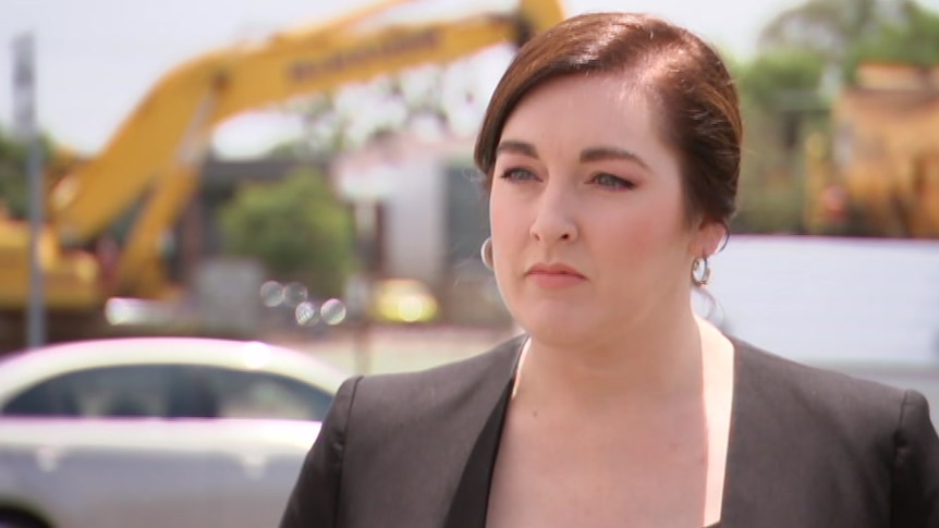 A woman with brown hair looks sternly at the camera wearing a black suit