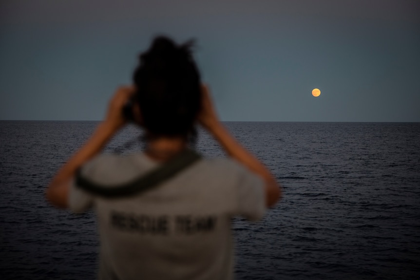 A woman looks over the water with binoculars.