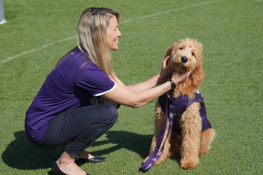 Angie Bain crouches next to Winnie the Groodle at Fremantle's training base in Cockburn